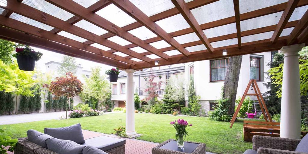 This is a picture of an arbor over a patio and landscaping in the background.